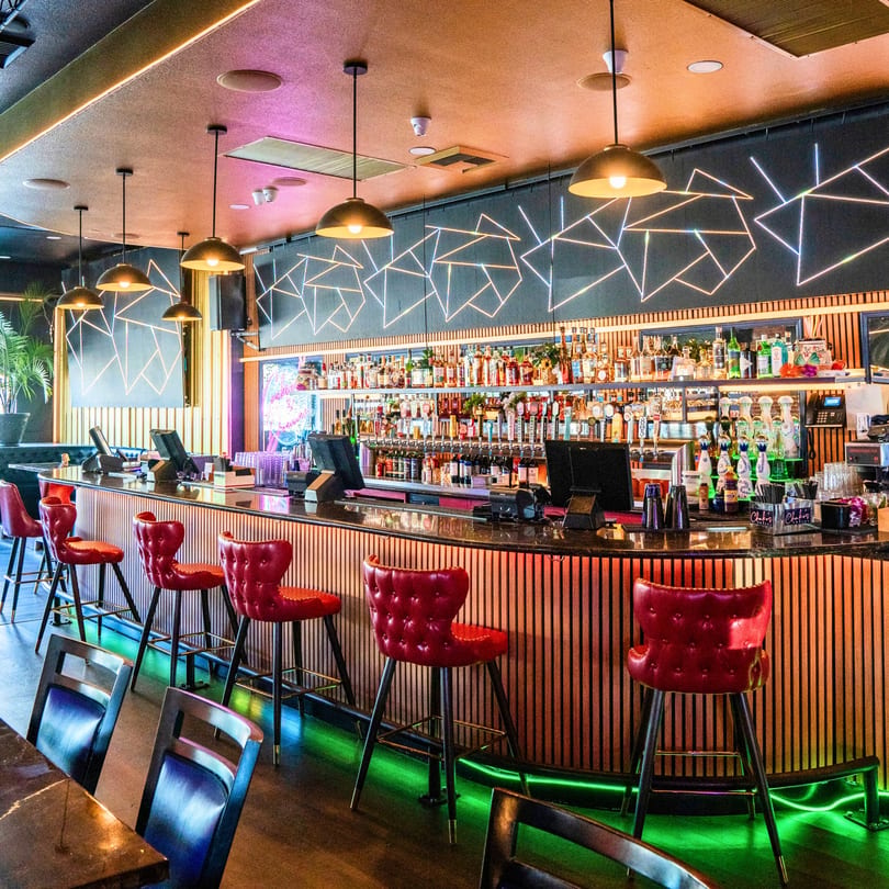 Chako's Social bar with red stools, a fully stocked liquor shelf, and neon lighting.
