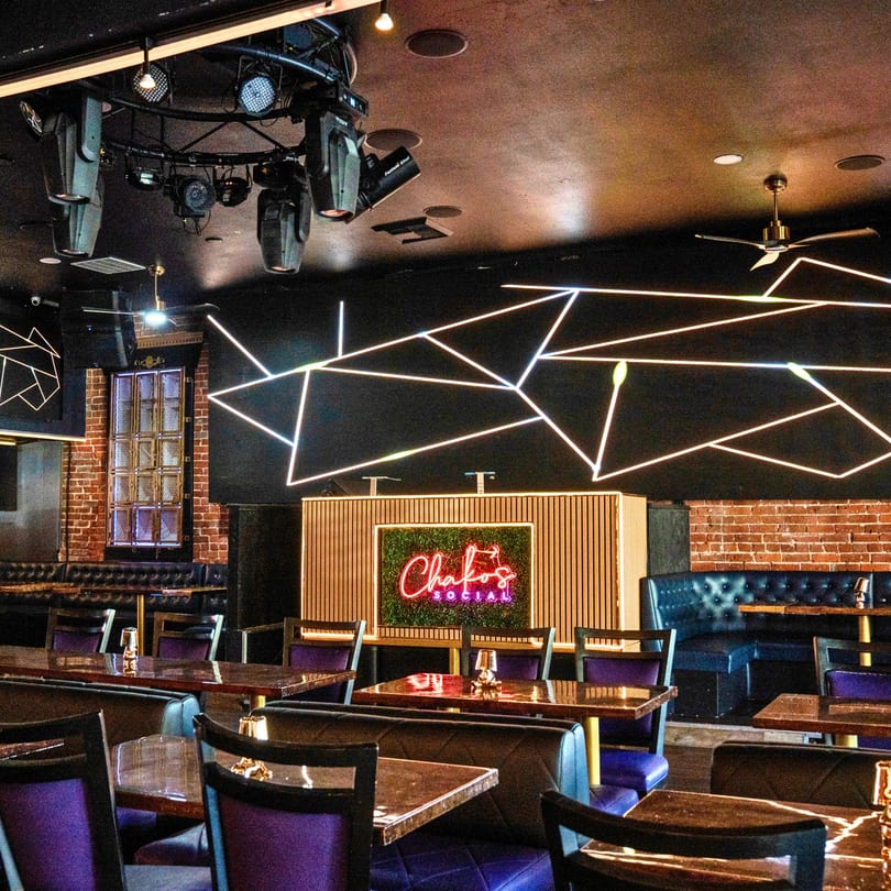 Chako's Social interior with neon lights, a DJ booth, and purple chairs at tables.